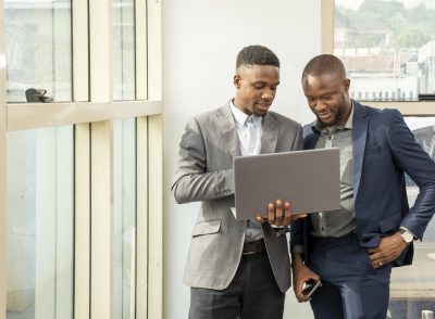 Two young black businessmen standing together holding a laptop, discussing business