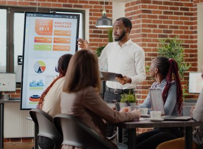 Company employee presenting business strategy with charts on monitor, planning project. Workmates analyzing financial statistics on display, working together on company development.